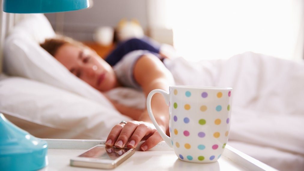 Woman in bed reaching for her mobile phone on nightstand